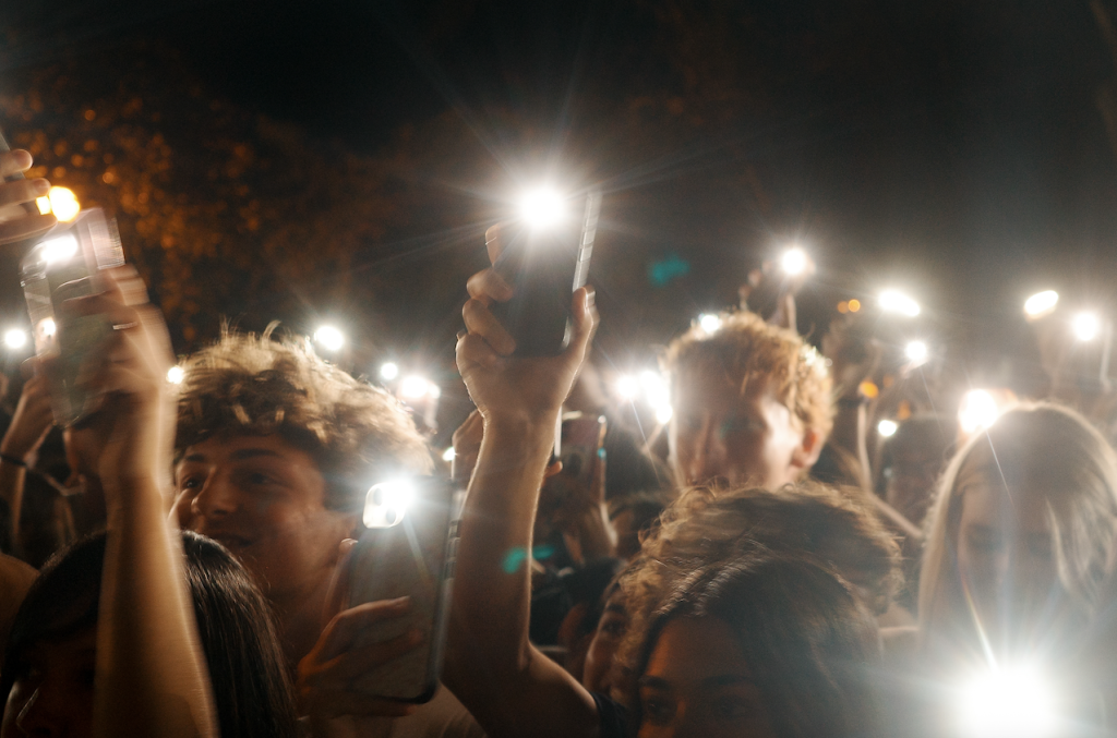 Close-up of crowd of students holding up phones with flashlights on.